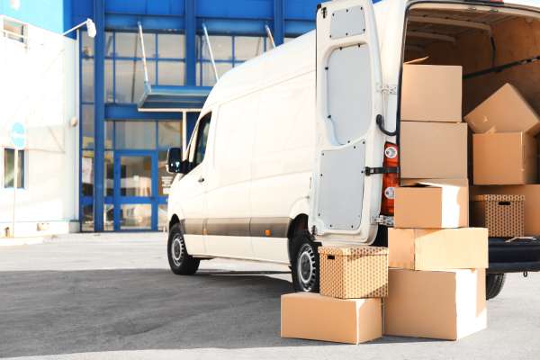 Boxes of items are being moved from a white van into a large commercial property.