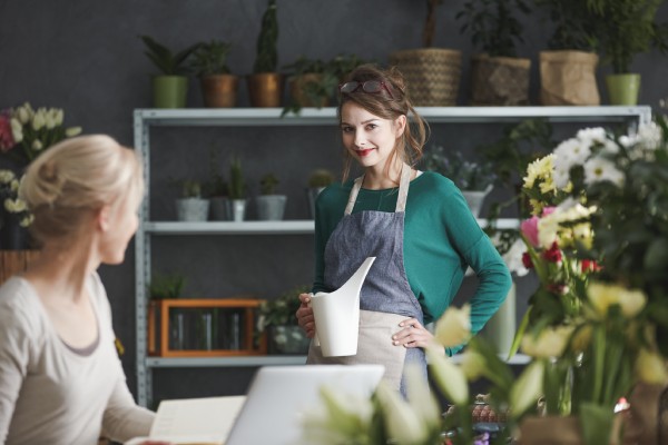 A female business owner stands in her plant shop and smiles proudly at the camera.