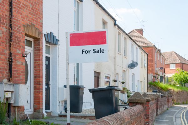 A "for sale" sign posted outside of a row of English terraced houses.