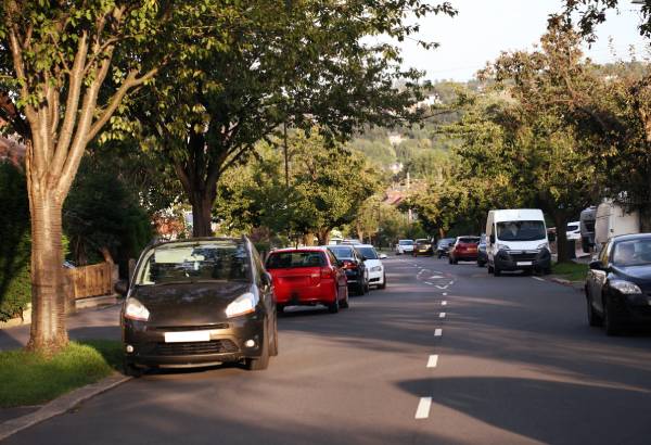 Cars parked on the side of a road in a residential area on a sunny day.